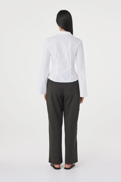 Full-length studio back view of a model wearing the white Arcaa Movement Ari Shirt, highlighting the back seam detailing, fitted silhouette, and dark grey trousers.