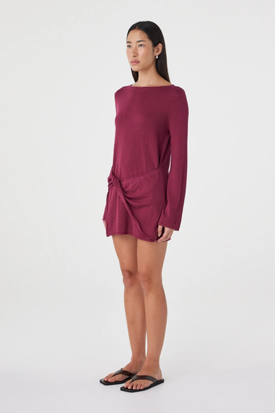 Three-quarter studio view of a model wearing the linen-cotton blend Arcaa Movement Kira Mini Dress in merlot, highlighting the side profile and twisted wrap panel.