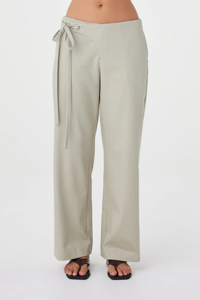 Cropped studio front shot of the Arcaa Movement Lucia Tie Pant in light sage, highlighting the silver eyelet and double tie asymmetrical waistband detail.