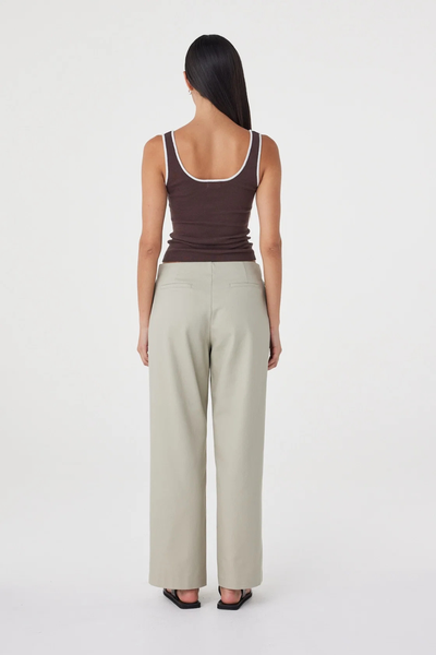 Full-length studio back view of a model wearing the light sage Arcaa Movement Lucia Tie Pant and a brown tank top with white trim.