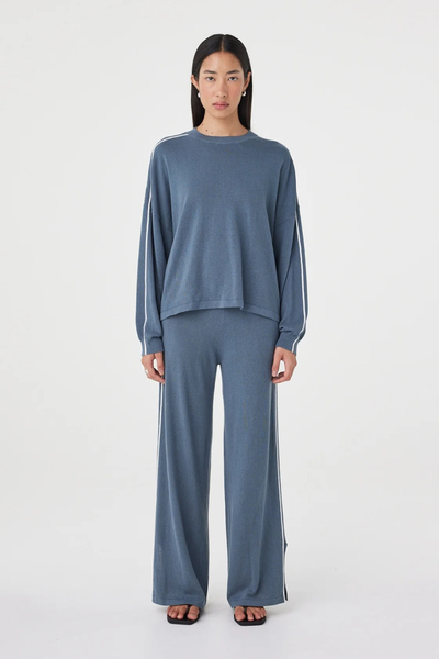 Full-length studio front view of a model in the storm blue Arcaa Movement Pippa Long Sleeve Tee set, showcasing the slouchy fit, crew neck, and cream side-stripe details.