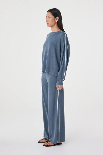 Three-quarter side studio view of a model wearing the storm blue Arcaa Movement Pippa Long Sleeve Tee, highlighting the drop shoulder seam and sleeve stripe accent.