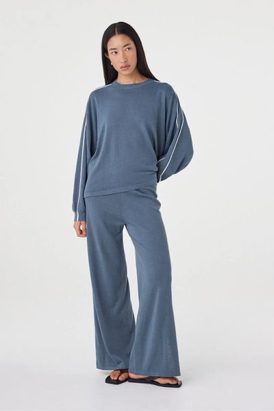 Full-length studio pose of a model wearing the storm blue Arcaa Movement Pippa Pant 2.0 and matching long-sleeve top with one hand behind her back.