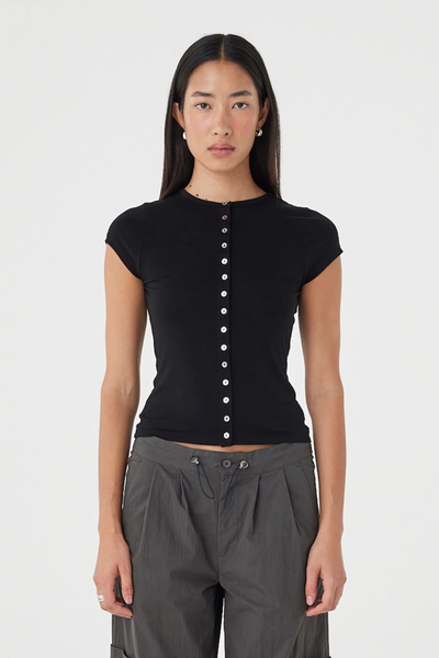 Front mid-shot studio view of a model in the black Arcaa Movement Robbie Top, highlighting the high crew neck, slim silhouette, and centre front button closure.