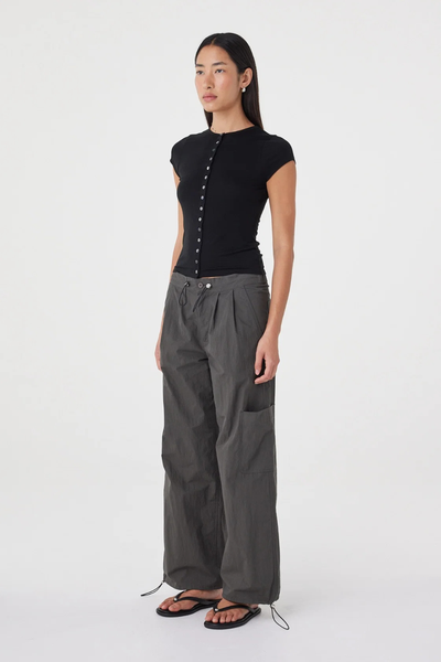Three-quarter studio view of a model wearing the fitted black Arcaa Movement Robbie Top, showcasing the side profile and body-skimming button-down design.