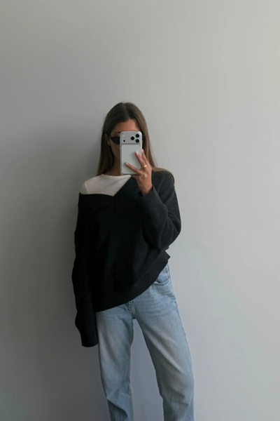 Mirror selfie of a woman wearing the dark grey marle Arcaa Movement Zenya Sweater layered over a white tee, styled casually with light wash jeans.
