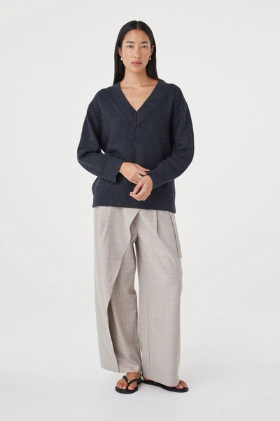 Full-length studio view of a model in the relaxed dark grey marle Arcaa Movement Zenya Sweater, styled with beige wrap front trousers and black sandals.