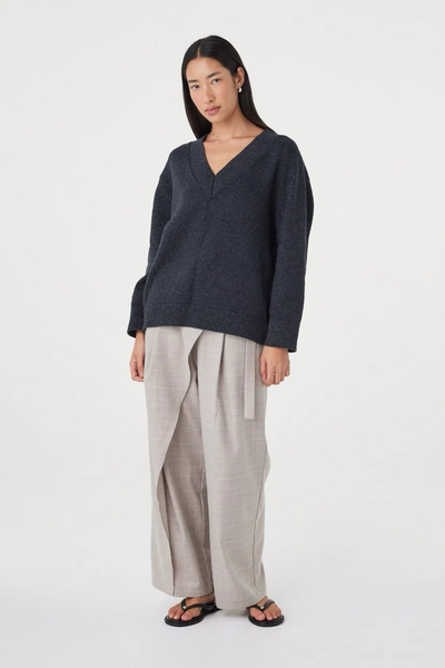 Full-length side-angle view of a model in the dark grey marle Arcaa Movement Zenya Sweater, highlighting the dropped shoulder design and fluid drape.