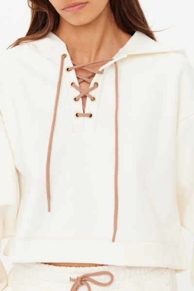 A close-up of the neckline featuring gold eyelets, a braided cream drawcord, and contrast mocha stitching.