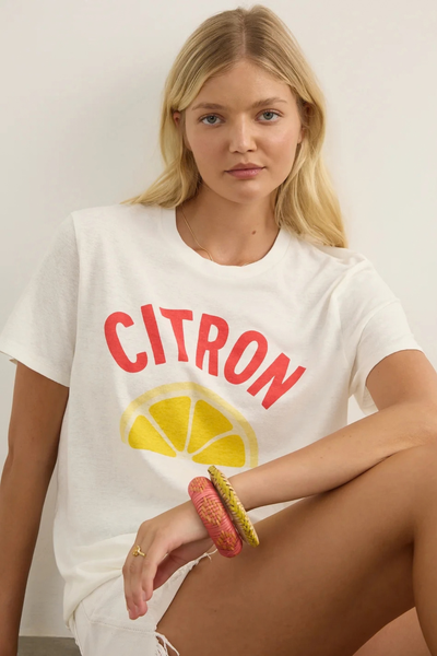 Studio close-up portrait of a model wearing the white t-shirt with red "CITRON" lettering and a yellow citrus slice graphic, accessorized with colorful woven bracelets.