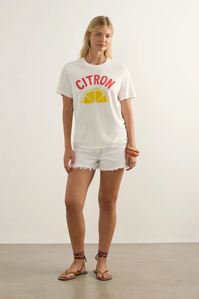 Studio front full-length view of a model wearing the white Citron graphic tee, white cutoff denim shorts, and strappy sandals.