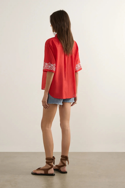 Studio rear view of a model wearing the red embroidered blouse, denim shorts, and brown lace-up sandals, highlighting the embroidered cuff detail.