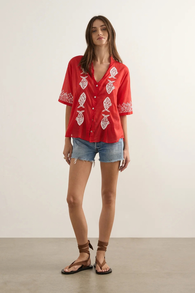 Studio front full-length view of a model wearing the oversized red blouse, denim shorts, and brown strappy sandals.