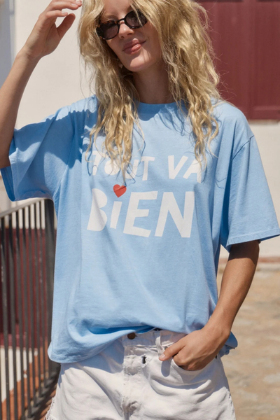 Close-up outdoor lifestyle portrait of a model wearing sunglasses and the sky blue boyfriend t-shirt paired with white shorts.