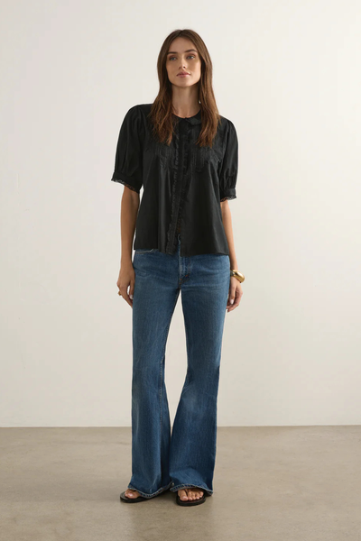 Full-length front studio shot of a model wearing the black cotton Magdalena Blouse paired with wide-leg blue denim jeans. This shot emphasizes the blouse's fluid, romantic drape, short puff sleeves, and relaxed vintage silhouette.