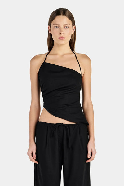 Studio mid-shot front view of a model wearing a black asymmetrical halter neck top with gathered side seams and an angled hemline.