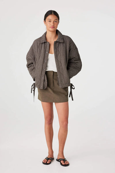 A full-length front view of the jacket worn open over a white tank top and olive mini skirt. The model is also wearing black studded sandals.