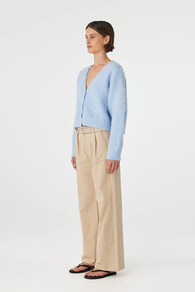 Side-profile studio shot of the Arcaa Movement Liora Fluffy Cardigan in Sky blue, showcasing the cropped length hemline and the clean, structured ribbing along the sleeve cuffs and lower hem. Styled with neutral tan tailored trousers.