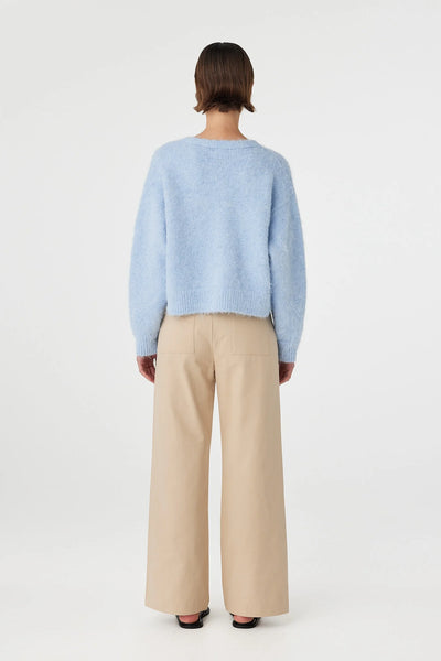 Full-length rear view of the Arcaa Movement Liora Fluffy Cardigan, highlighting the clean, slouchy drape across the shoulders and back. The pastel sky blue knit is paired with wide-leg beige trousers featuring classic square back patch pockets.
