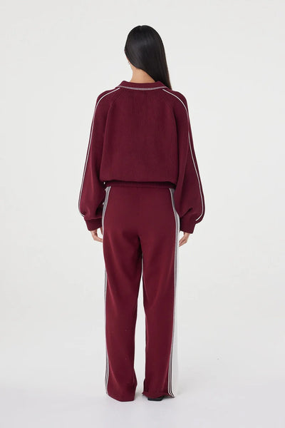 A full-length studio shot from behind, showing the back profile of the Emery Pant. This angle emphasizes the clean, streamlined silhouette and the cream contrast sporty side stripe running down the length of each leg.