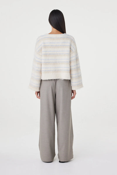 A full-length studio shot from behind, showing the back profile of the Lucca Sweater. This angle displays the soft cropped shape, relaxed drape, and the continuous custom taupe and blue horizontal stripe artwork running across the shoulders and fluid wide sleeves.