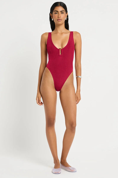 Full-length studio front view of a model wearing mesh shoes and the wine red shimmer cord ribbed one-piece swimsuit featuring a plunge neck with ring detail.