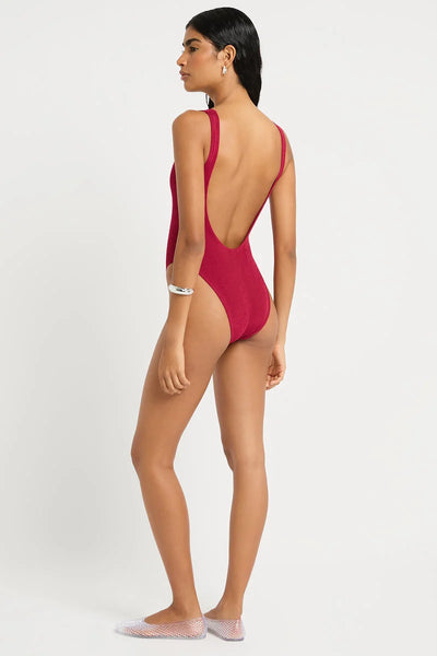 Studio rear three-quarter view of a model wearing a wine red shimmer cord crinkle-textured one-piece swimsuit, showcasing the low open back line.