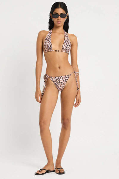 Full-length studio front view of a model wearing dark sunglasses and the reversible beaded triangle top and side-tie briefs on the printed papillon side.