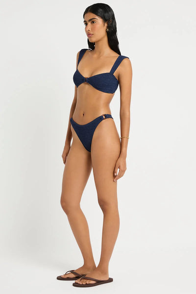 Full-length studio front view of a model wearing flat flip-flops and the dark navy nocturne shimmer crinkle-textured Ring Scene Brief with side resin rings and a curved waistline.
