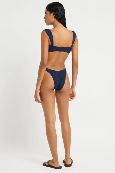 Studio rear three-quarter view of a model wearing dark navy shimmer crinkle-fabric crop bikini top and high-cut briefs, showcasing the straight back band.