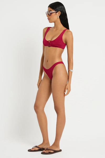 Studio three-quarter front view of a model wearing the wine red shimmer cord ribbed bikini briefs styled on a high-leg fit.