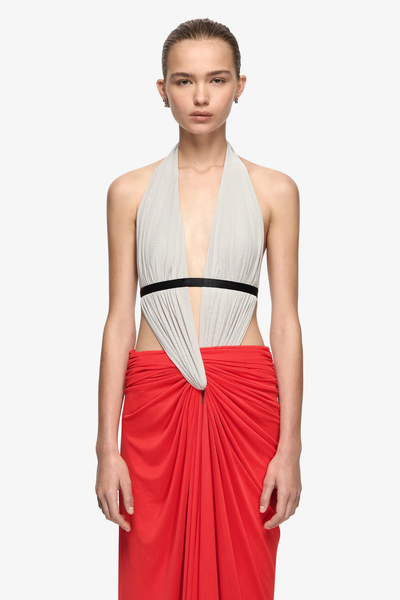 Studio three-quarter front view of a model wearing a soft mesh maxi dress featuring a dove grey plunging halter neckline, black elastic underbust band, and flame red center-tuck draped skirt.