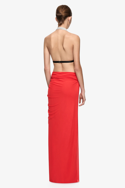 Studio rear full-length view of a model wearing a backless soft mesh maxi dress highlighting the thin black underbust strap with hook-and-eye closure and low flame red skirt waist.