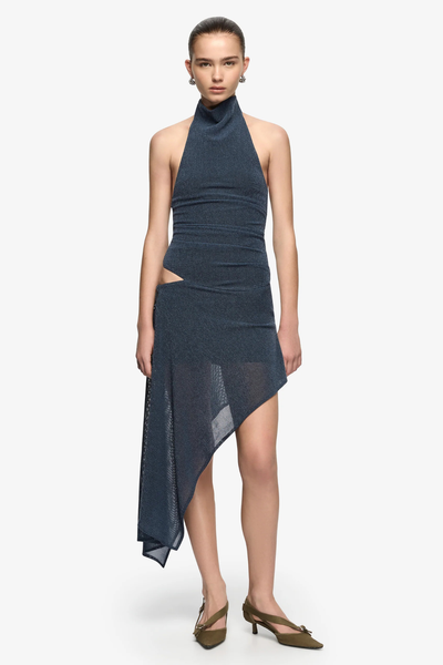 Full-length studio front shot of a model wearing a denim marle mini dress featuring the hip tie worn untied into an asymmetrical long side drape, styled with pointed olive heels.