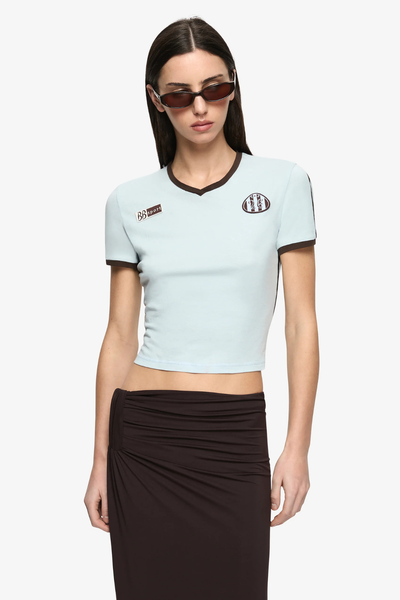 Waist-up front studio shot showcasing the baby tee's V-neckline, chocolate contrast binding, and chest embroidered patches.