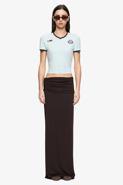 Full-body front studio view of a model wearing the Bec + Bridge Solara Tee in Sky Blue/Chocolate paired with a long dark brown skirt and sunglasses.