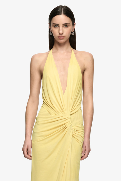 Three-quarter front studio view of a model wearing a citron yellow backless maxi dress highlighting the deep plunging neckline and gathered waist knotting.