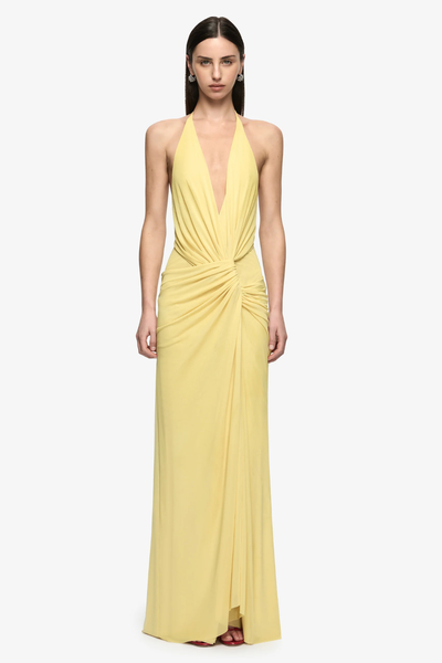 Studio full-length front view of a model wearing a citron yellow draped backless maxi dress with a plunging V-neckline and gathered waist detail styled with red heels.