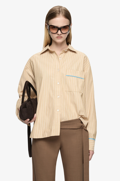 Waist-up studio shot showcasing the oversized fit, button placket, and blue contrast binding on the chest pocket.