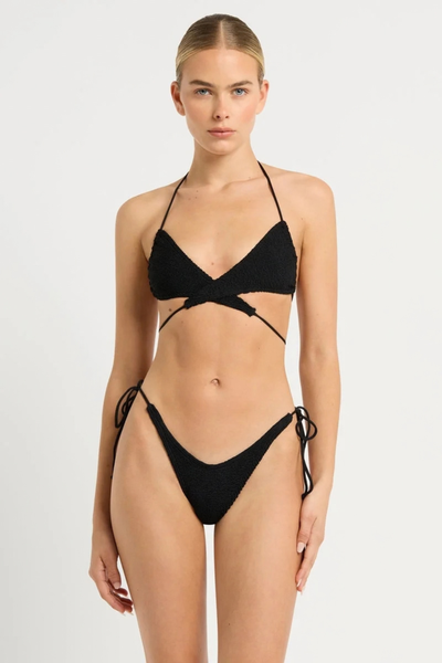 Studio front view of a model wearing a black crinkle triangle bikini styled with the ties wrapped cross-front around the waist.