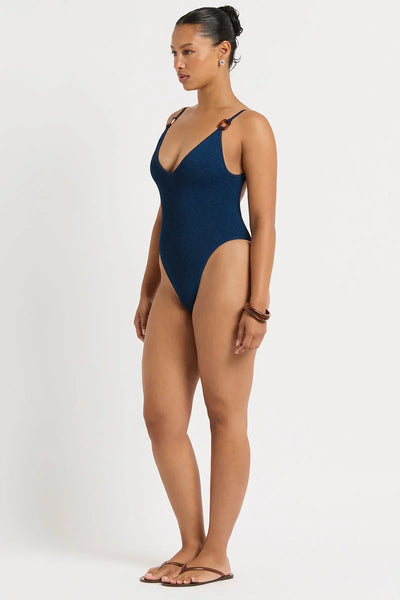 Side profile view of model Yaz wearing the Bond-Eye Ring Elena Marine Recycled crinkle one-piece swimsuit featuring thin shoulder straps and high leg line.
