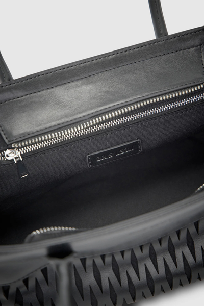 Interior detail view of the open black Brie Leon Faye Mini Tote, showing the black cotton twill lining, internal wall zip pocket with silver pull, and debossed logo badge.