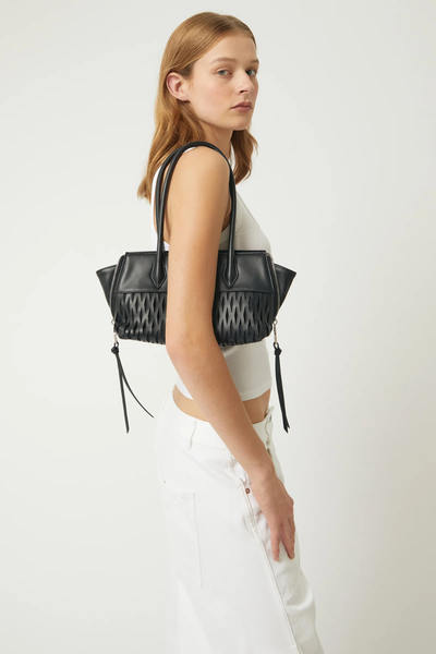 Side profile model shot of the black Brie Leon Faye Mini Tote worn over the shoulder, styled with a white ribbed tank top and casual white trousers.
