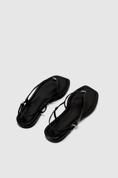 Angled product shot of the pair of black flat sandals showing the slingback buckle closure and minimal profile.