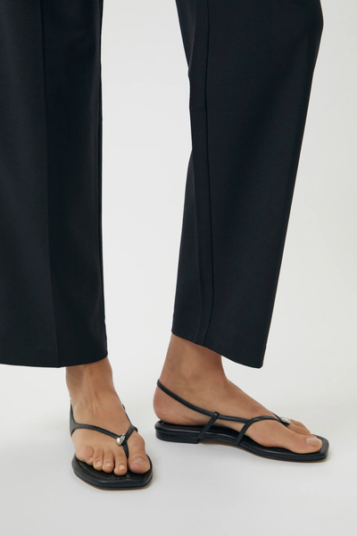 Low-angle product shot focusing on the fit of the black sandals worn with cropped trousers.