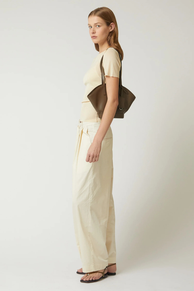 Full-length side profile shot of a model wearing the forest green Brie Leon Heather Mini Tote over the shoulder, styled with a cream short-sleeve top and wide-leg trousers.