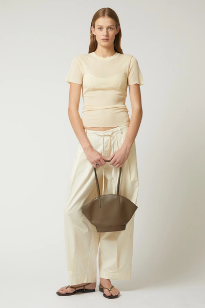 Full-body front shot of a model holding the forest green Brie Leon Heather Mini Tote by its top handles in front of a neutral backdrop.