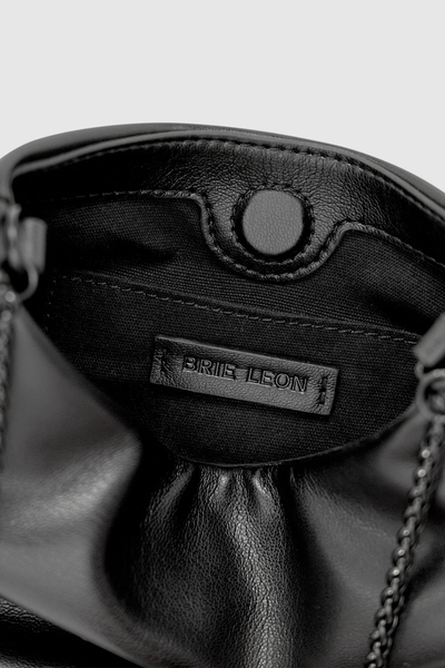 Close-up interior view of the Brie Leon Iris Mini Bag in black showing the hidden magnetic dot closure, black 100% recycled cotton twill lining, and stitched leather brand logo patch.