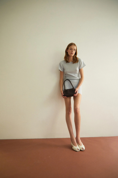 Full-length studio portrait of a model posing against a neutral backdrop while holding the dark chocolate mini bag.