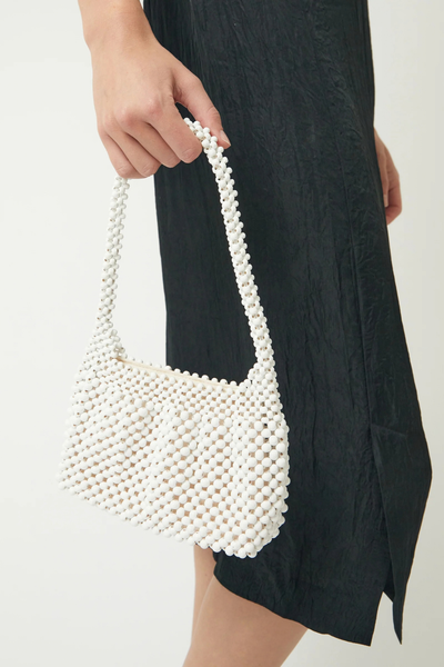 Close-up handheld shot of the structured oat beaded mini bag, highlighting the intricate handwoven wooden beadwork and sculptural top handle.